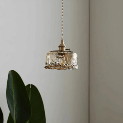 Vintage-style pendant light with glass shade and brass fixture against a neutral wall.