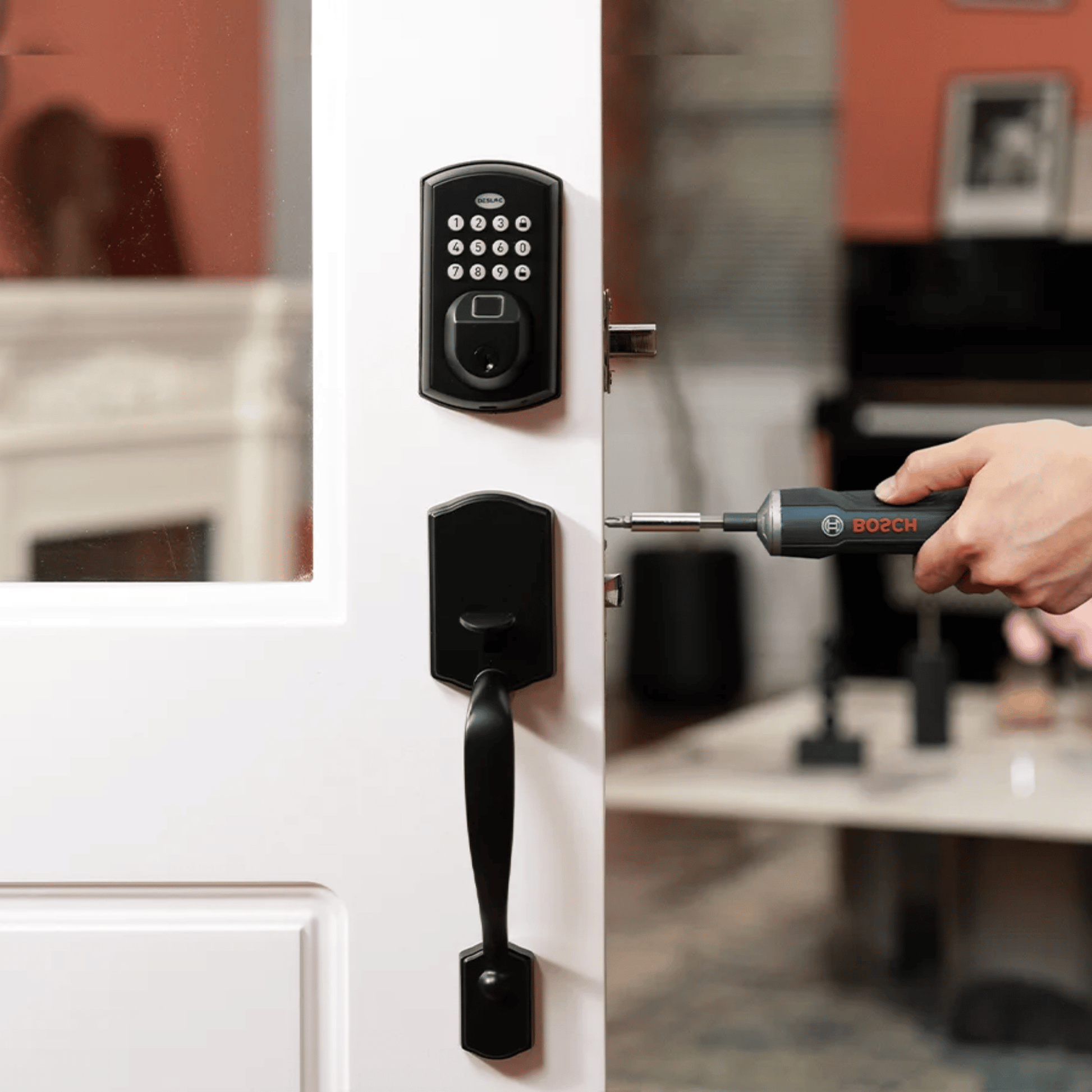 Person using a screwdriver to adjust a black electronic door lock on a white door.
