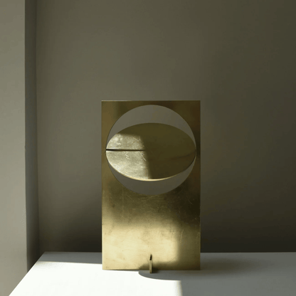 Gold abstract sculpture on a gray surface with a dark background