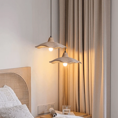 Two pendant lights hanging above a bed with beige curtains in the background.