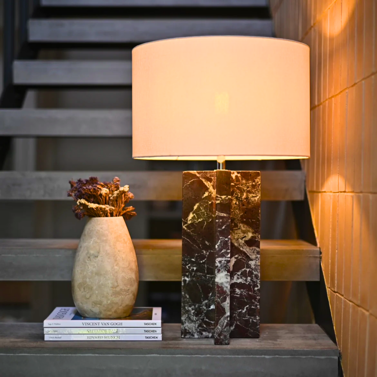 Table lamp with marble base on a step next to a vase and books