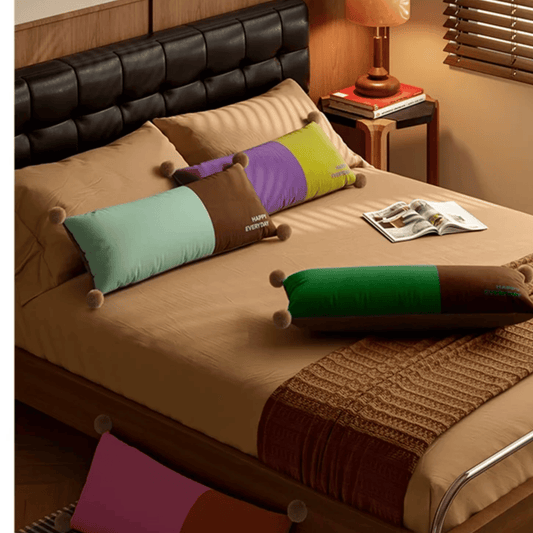 Bed with colorful pillows and a magazine on a wooden nightstand.