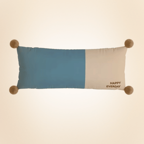 Color-blocked pillow with pom-pom accents and 'Happy Everyday' text on a beige background