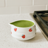 White ceramic pitcher with strawberry design filled with green liquid on a kitchen counter.