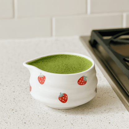 White ceramic pitcher with strawberry design filled with green liquid on a kitchen counter.