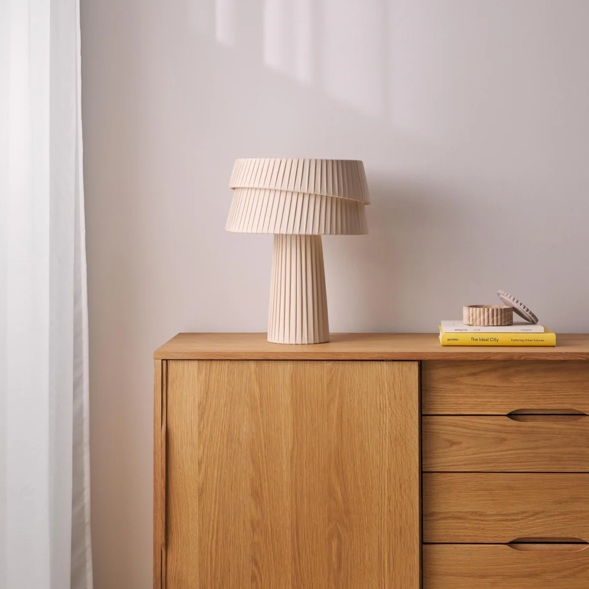 Wooden sideboard with a lamp and books against a plain wall
