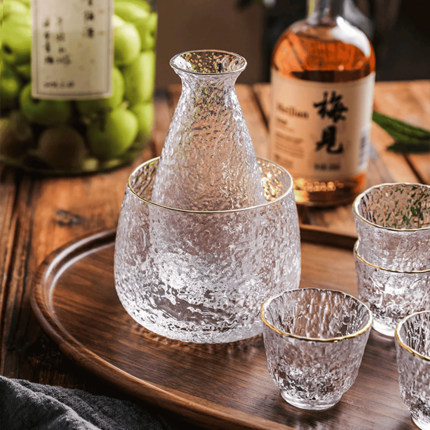 Clear glass sake set with a wooden tray and bottles in the background