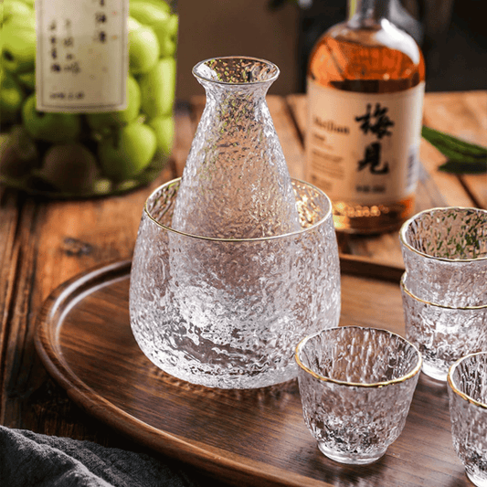 Clear glass sake set with a wooden tray and bottles in the background