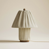 Table lamp with a pleated beige base and shade on a plain background
