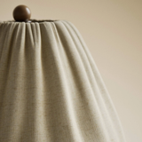 Close-up of a textured beige lampshade with a wooden finial on a neutral background