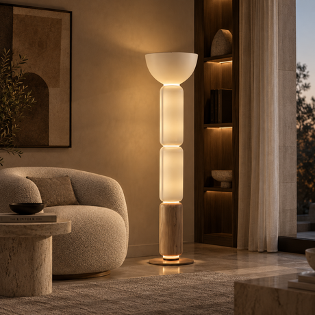 A modern multi-tiered floor lamp with a white bowl-shaped top, three glowing cylindrical shades, and a light wood base, standing in a warmly lit living room next to a curved beige sofa.