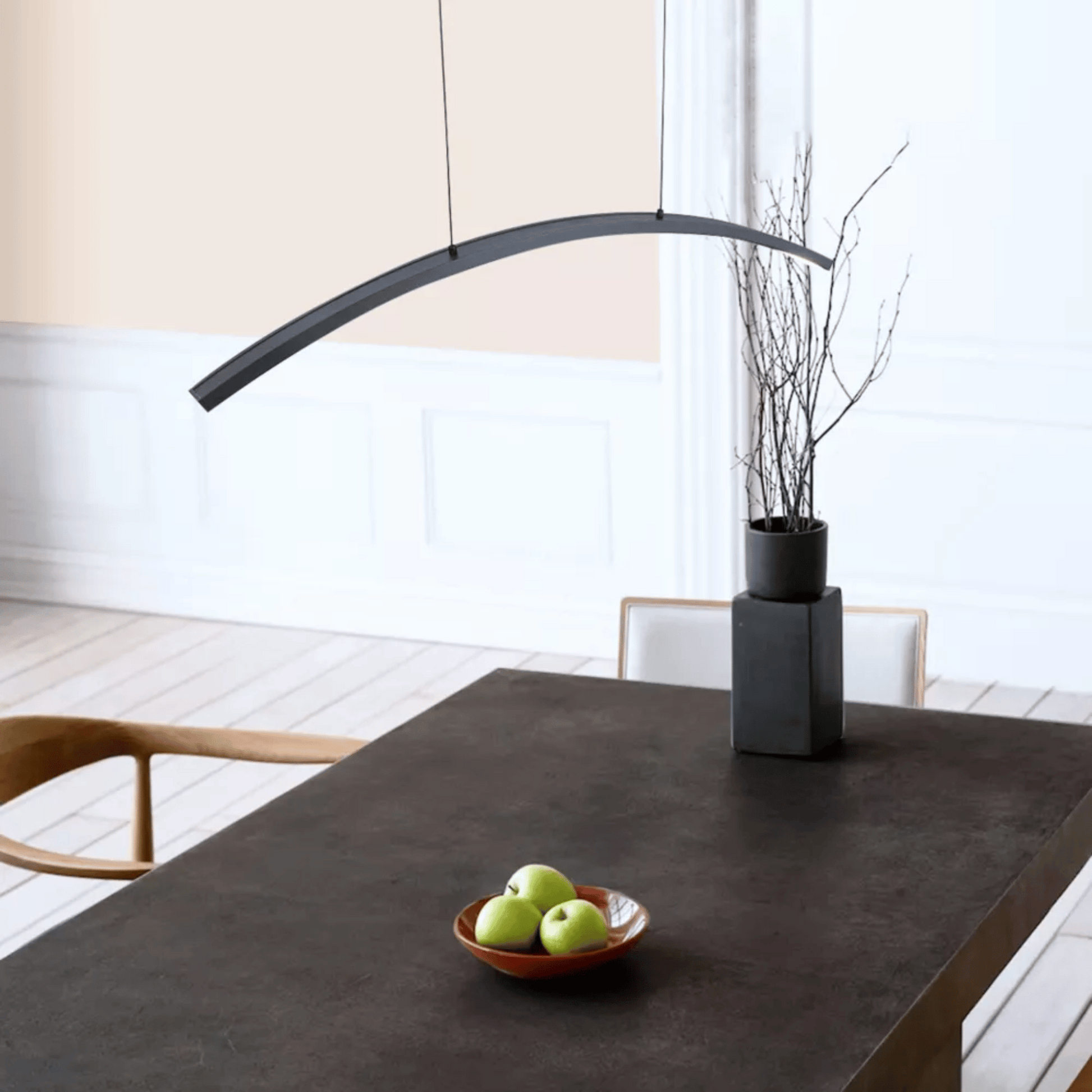 Modern dining table with a bowl of apples and a vase in a minimalistic room.