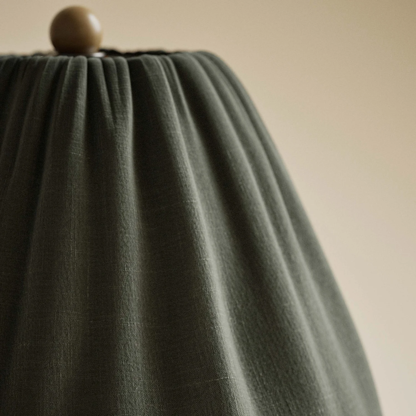 Close-up of a green lampshade with a wooden finial on a beige background