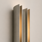 Modern wall-mounted light fixture with a metallic finish on a neutral background