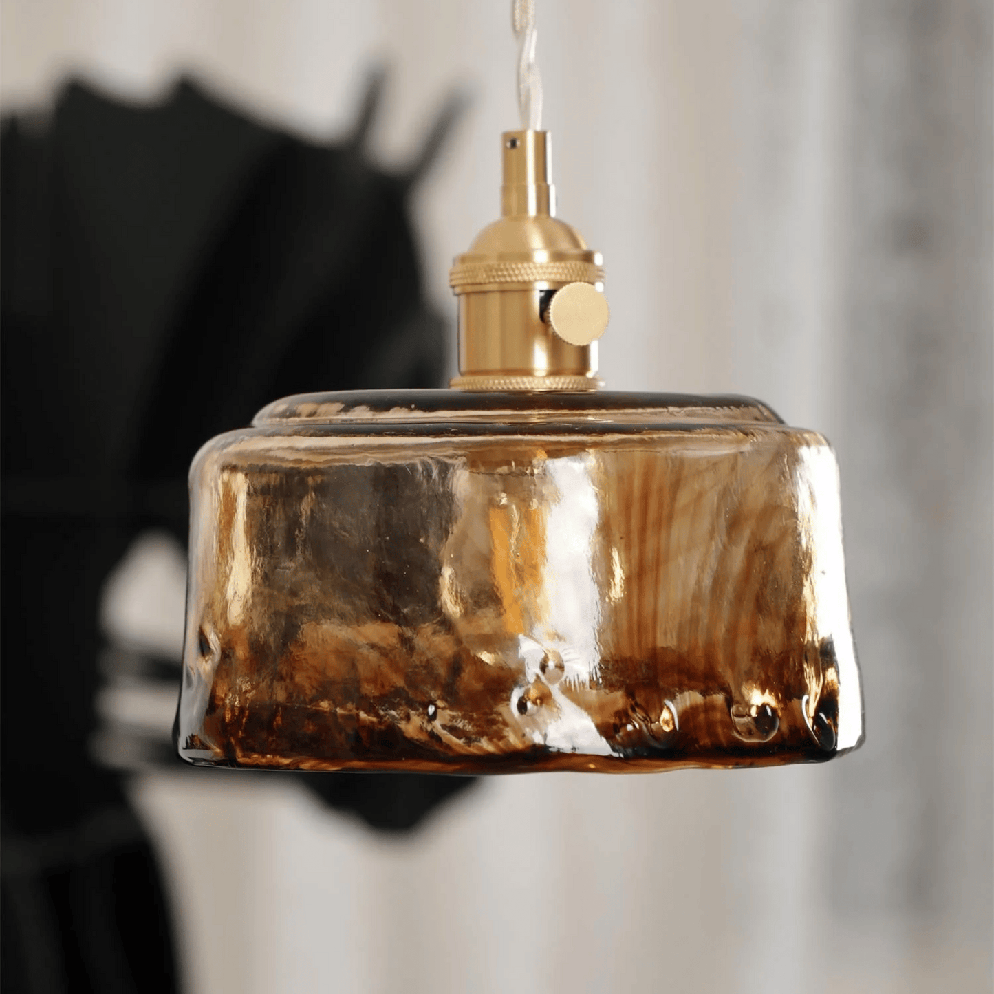 Decorative pendant light with a brown glass shade and gold metal fixture against a blurred background.