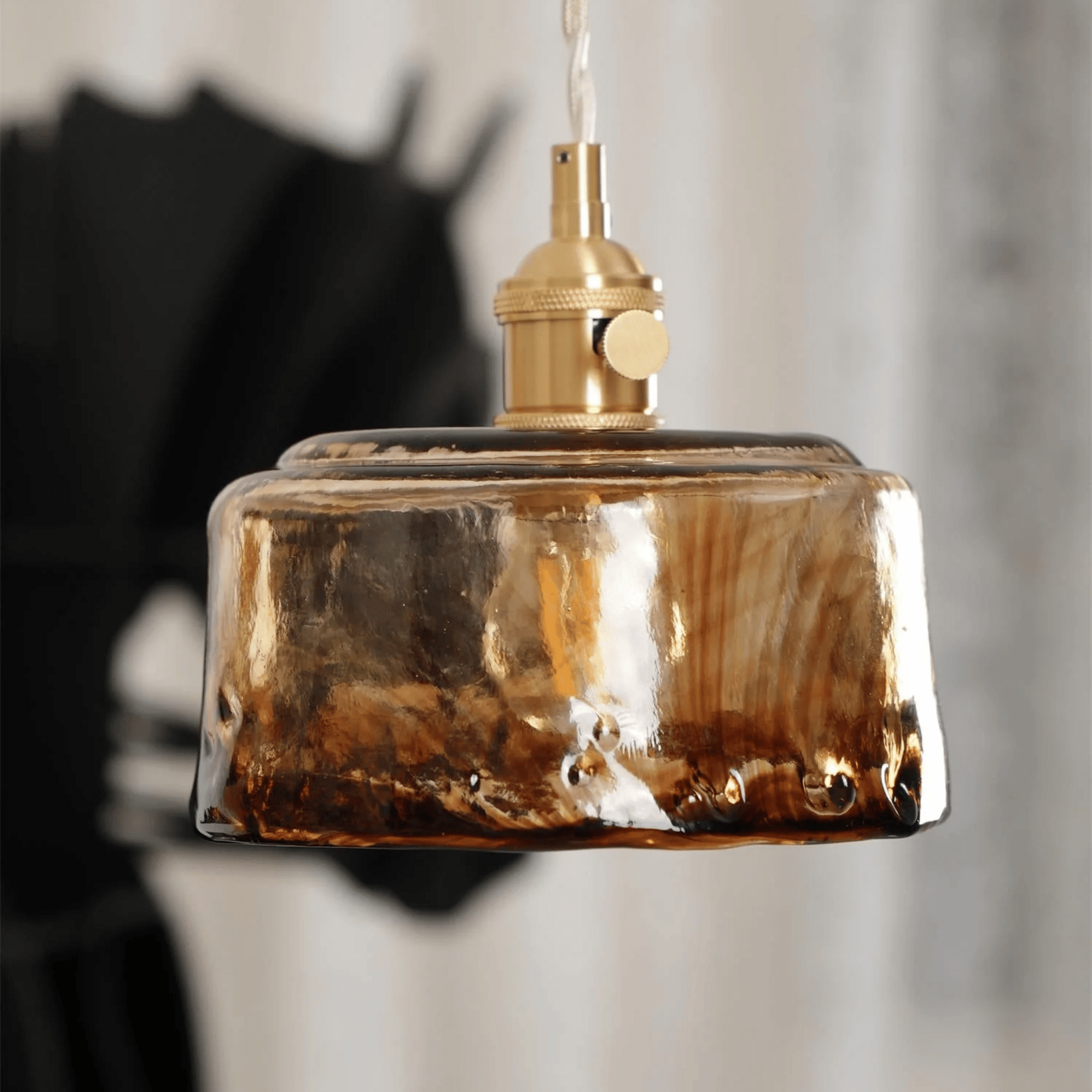 Decorative pendant light with a brown glass shade and gold metal fixture against a blurred background.