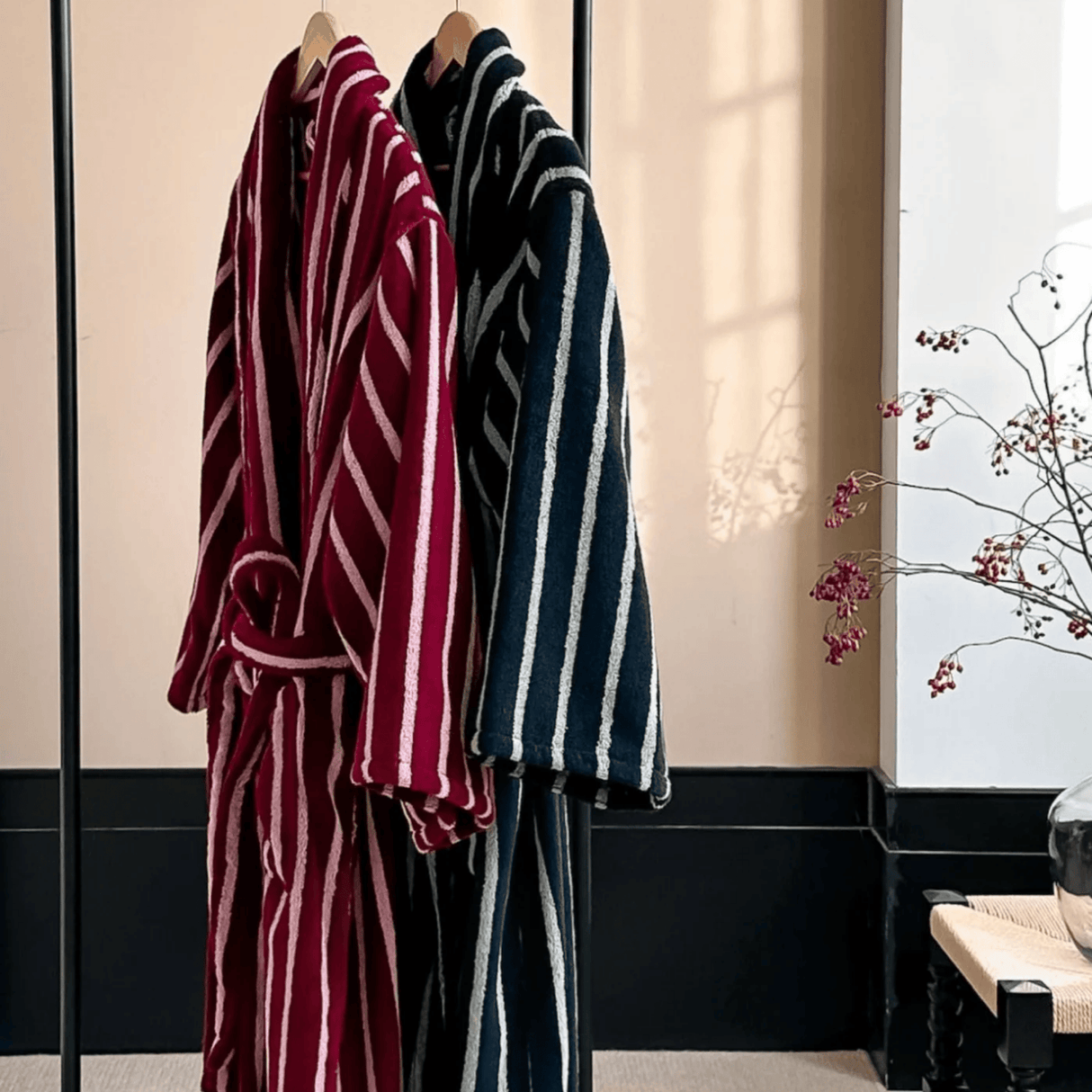 Two striped bathrobes, one red and white, one blue and white, hanging in a room with a decorative plant.