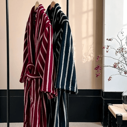 Two striped bathrobes, one red and white, one blue and white, hanging in a room with a decorative plant.