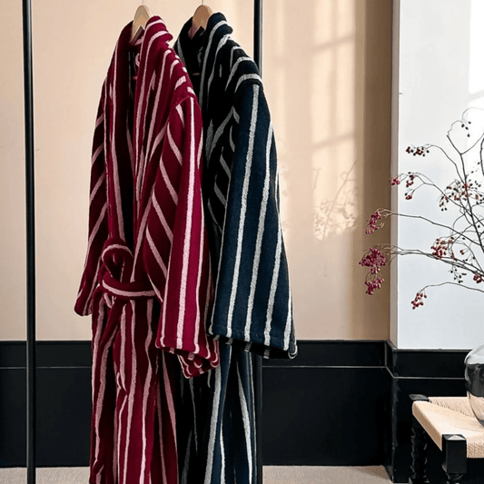 Two striped bathrobes, one red and white, one blue and white, hanging in a room with a decorative plant.
