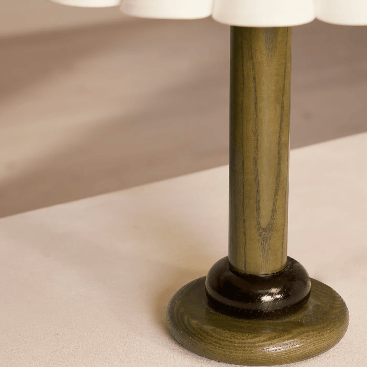 Close-up of a table lamp with a wooden base and white shade on a beige surface.