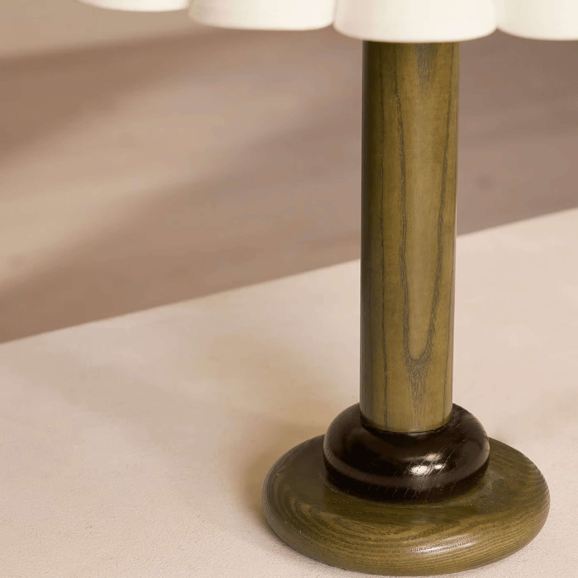 Close-up of a table lamp with a wooden base and white shade on a beige surface.