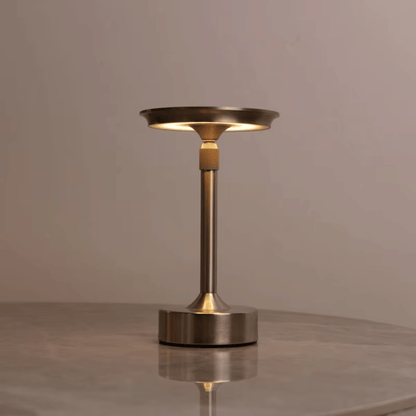 Modern table lamp with bronze finish on a reflective surface and neutral background