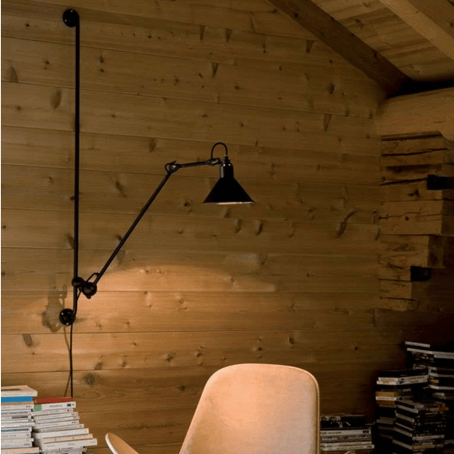 Black adjustable wall lamp in a room with wooden walls and books.