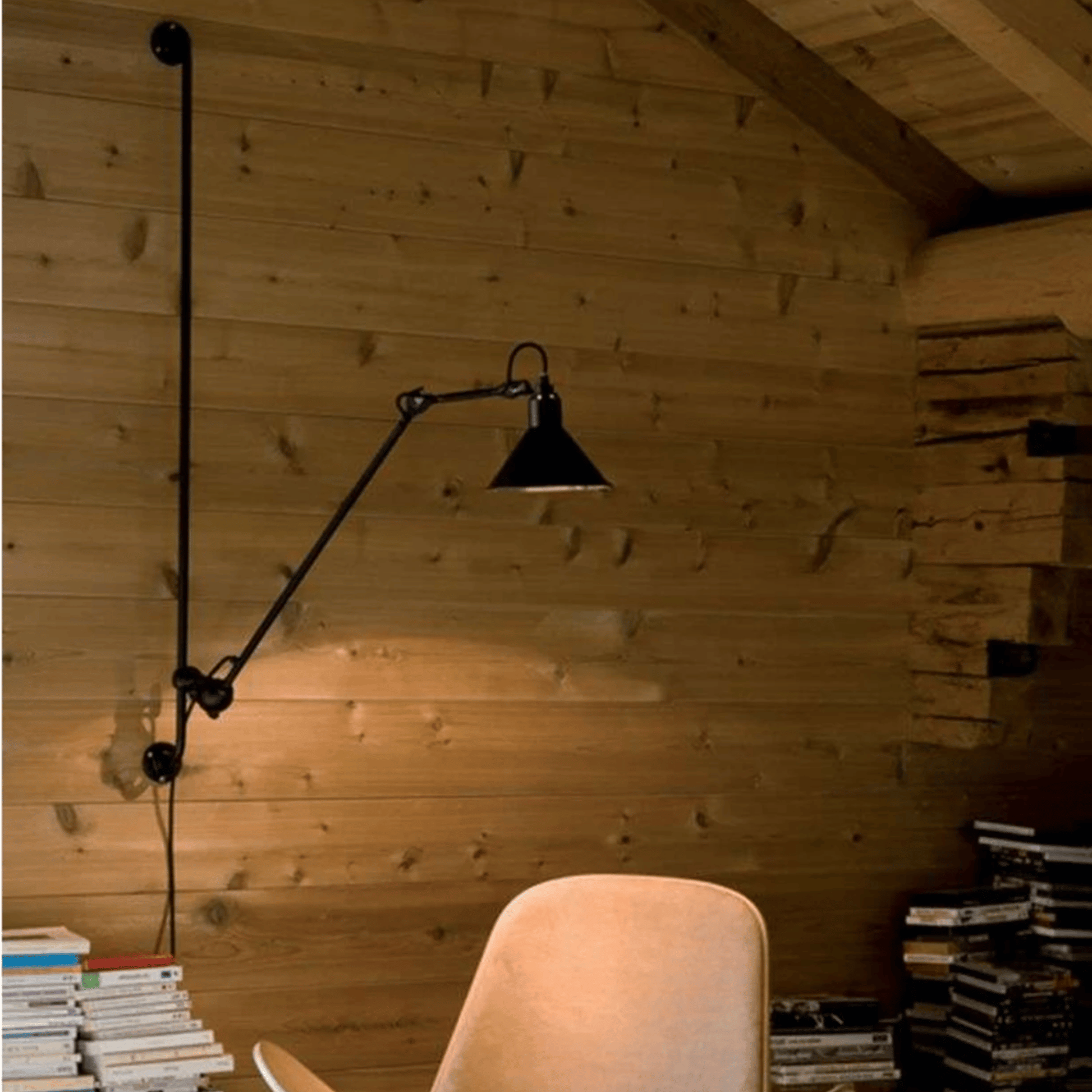 Black adjustable wall lamp in a room with wooden walls and books.