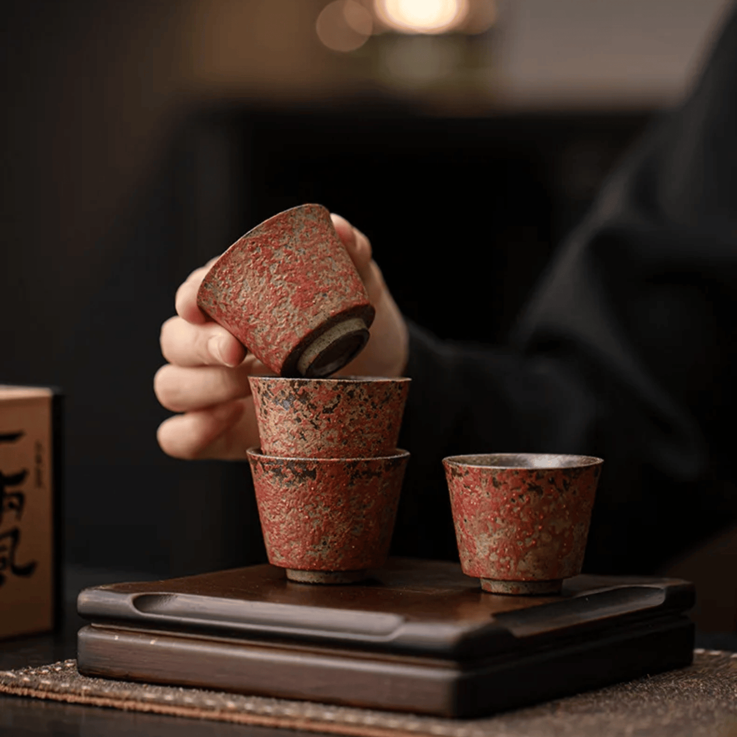 Person stacking ceramic cups on a wooden tray with a blurred background