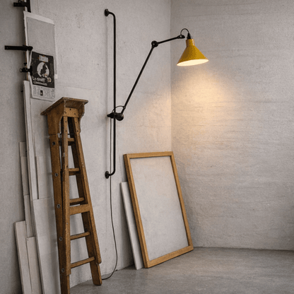 Yellow wall lamp with black arm next to a wooden ladder and large mirror against a gray brick wall.