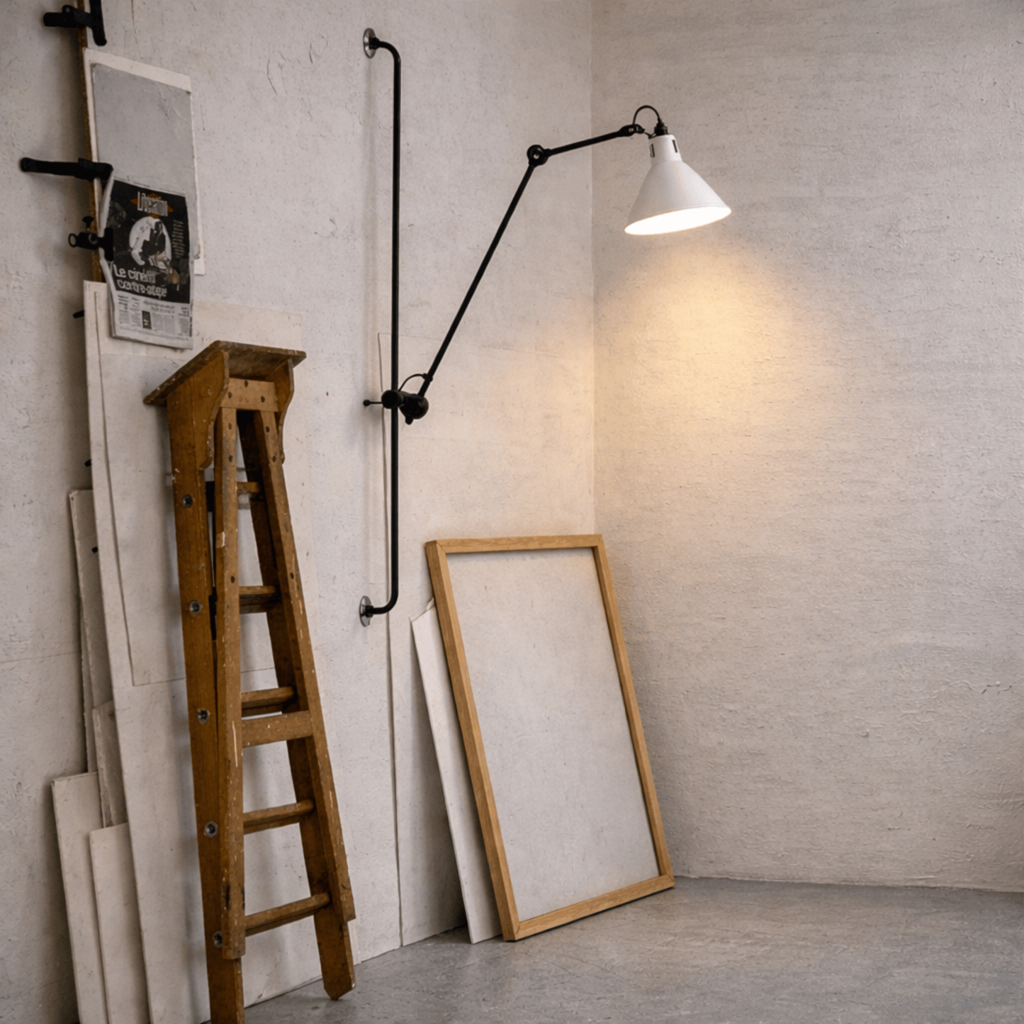 Wall lamp with a long arm next to a wooden ladder and framed mirrors against a textured wall.