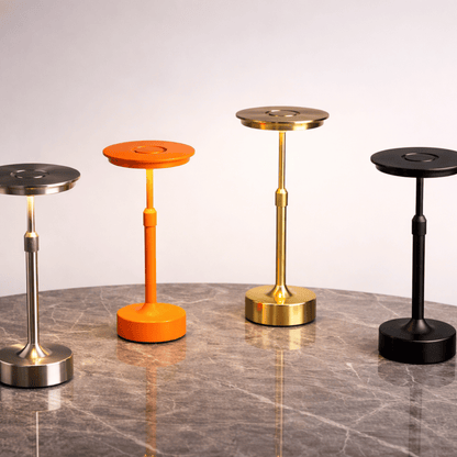 Four modern stools in different colors (silver, orange, gold, black) on a reflective surface with a neutral background.
