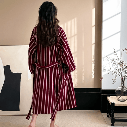 Woman wearing a burgundy and white striped robe in a room with a window and black coat on a stand.