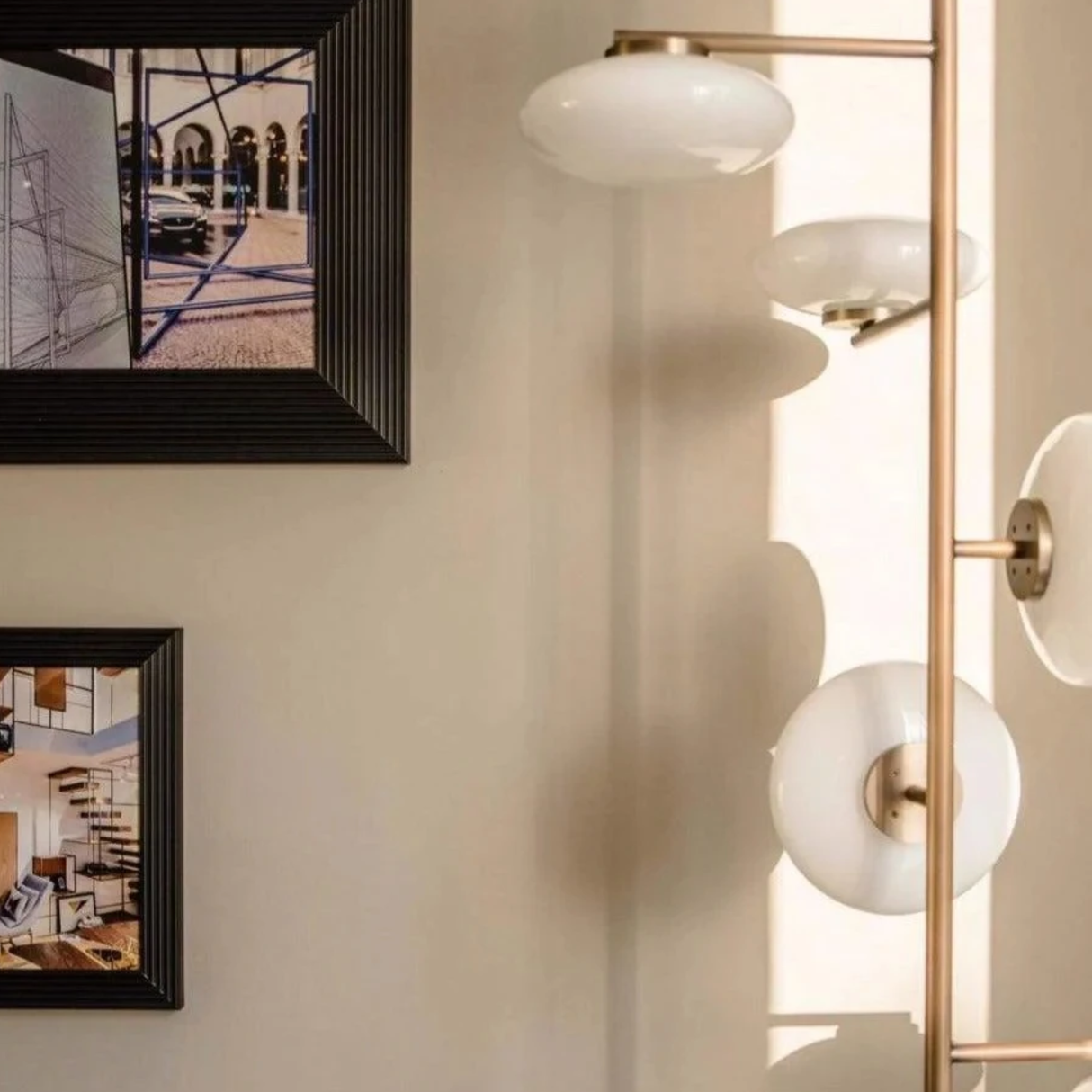 Modern wall-mounted light fixture with spherical glass shades in a room with framed artwork on the wall.