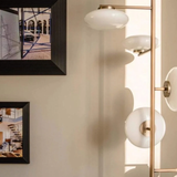 Modern wall-mounted light fixture with spherical glass shades in a room with framed artwork on the wall.