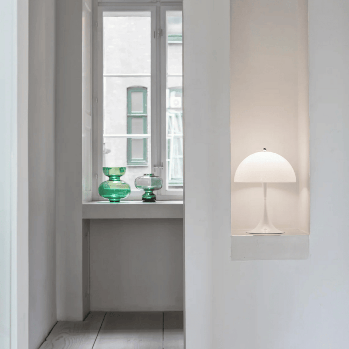 Modern interior with a white lamp and green glass vases on a windowsill.