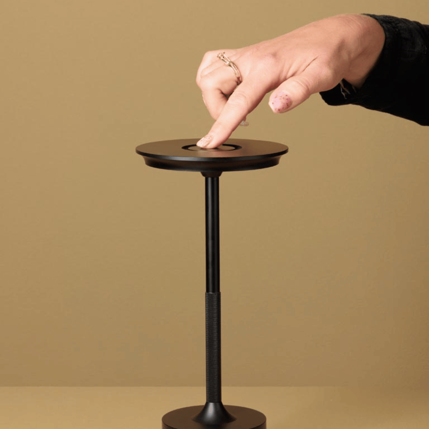Hand pressing a button on a small round table against a beige background