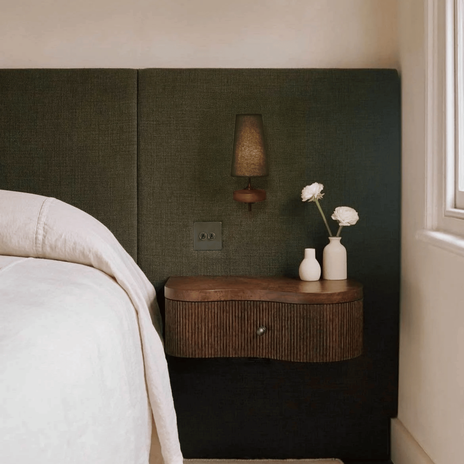 Bedroom with a wooden nightstand against a dark green headboard.