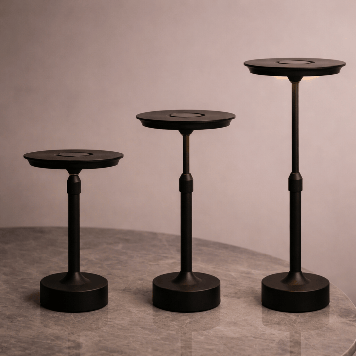 Three black pedestal tables of varying heights on a gray surface with a neutral background