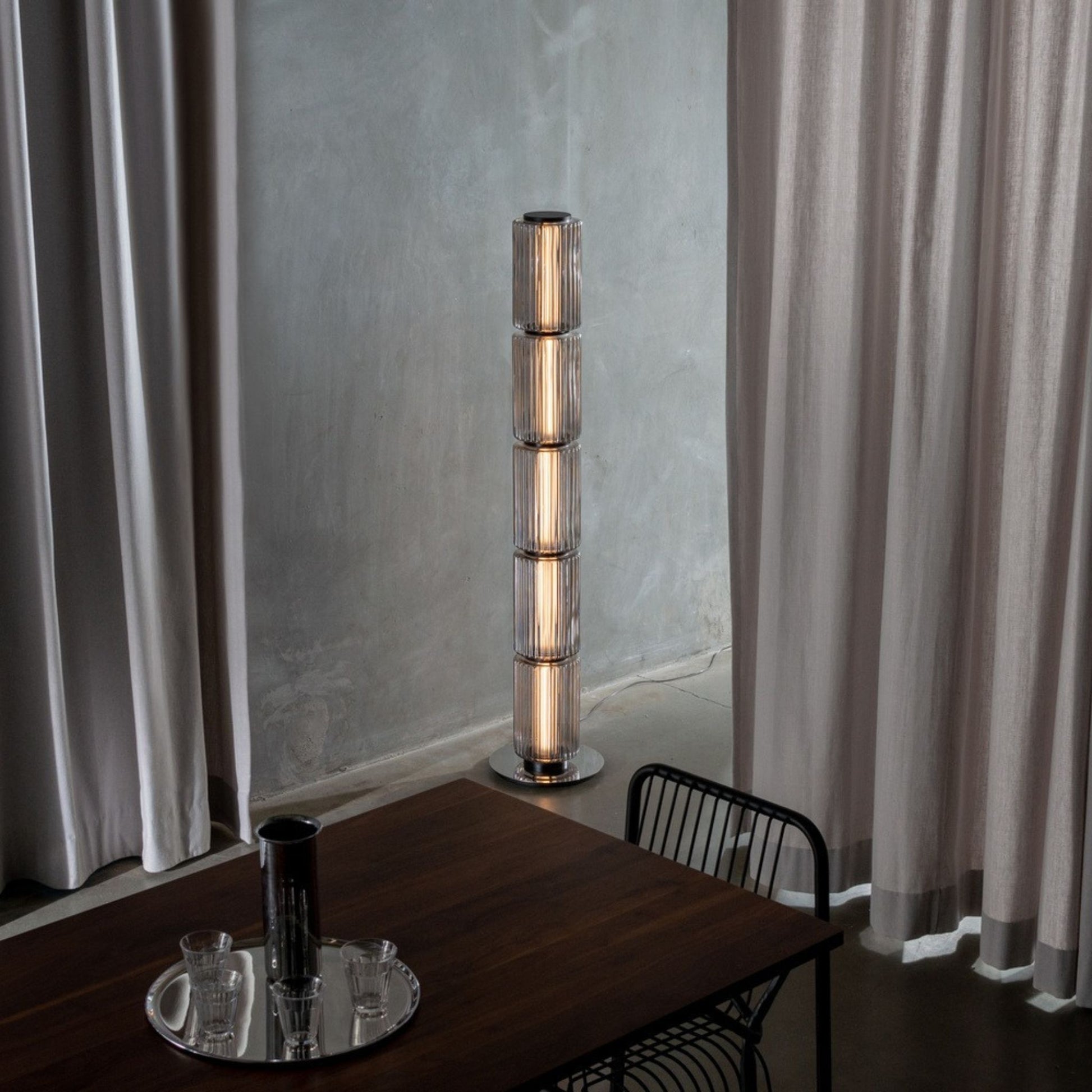 Tall glowing floor lamp standing on an orange carpet in a spacious interior.