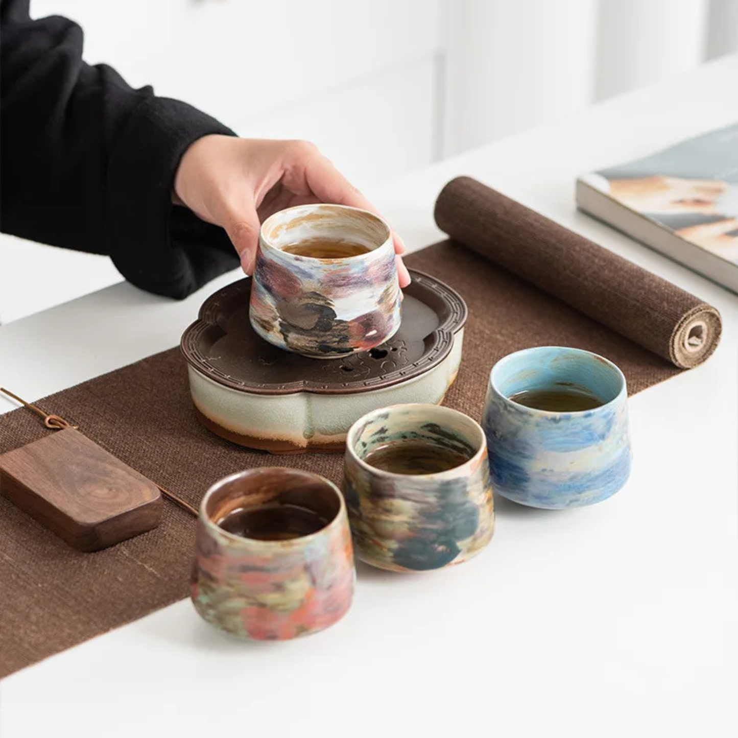 Set of four handcrafted ceramic cups in various multicolor glazes arranged on a tea table during a serving session.