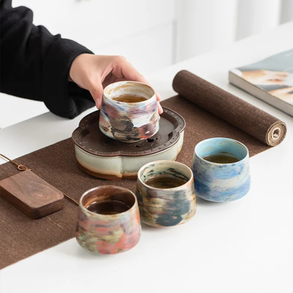 Set of four handcrafted ceramic cups in various multicolor glazes arranged on a tea table during a serving session.