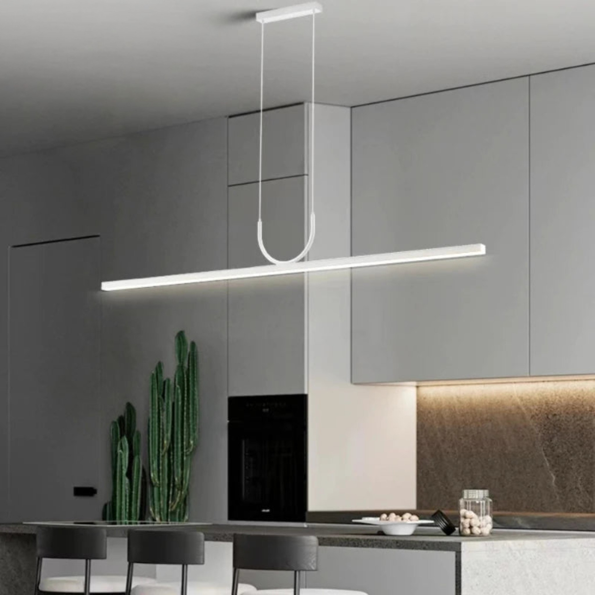 A minimalist contemporary kitchen featuring white cabinetry, a wooden open shelf, a compact white microwave, and two rattan chairs set around a small dining table illuminated by a stylish black pendant light.