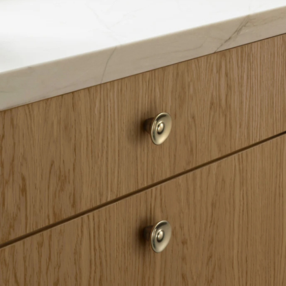 Metallic round cabinet knobs installed on wooden drawers under a marble countertop