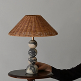 Hand adjusting the lamp on a wooden surface, showing its compact and earthy design.