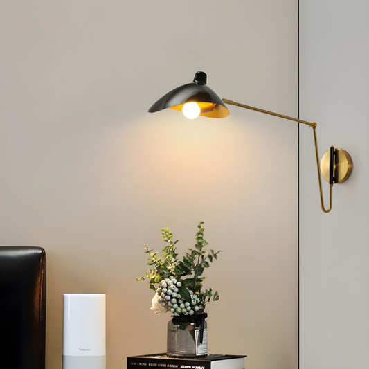 Sleek black and gold swing-arm wall lamp above a nightstand with flowers, illuminating the space softly.