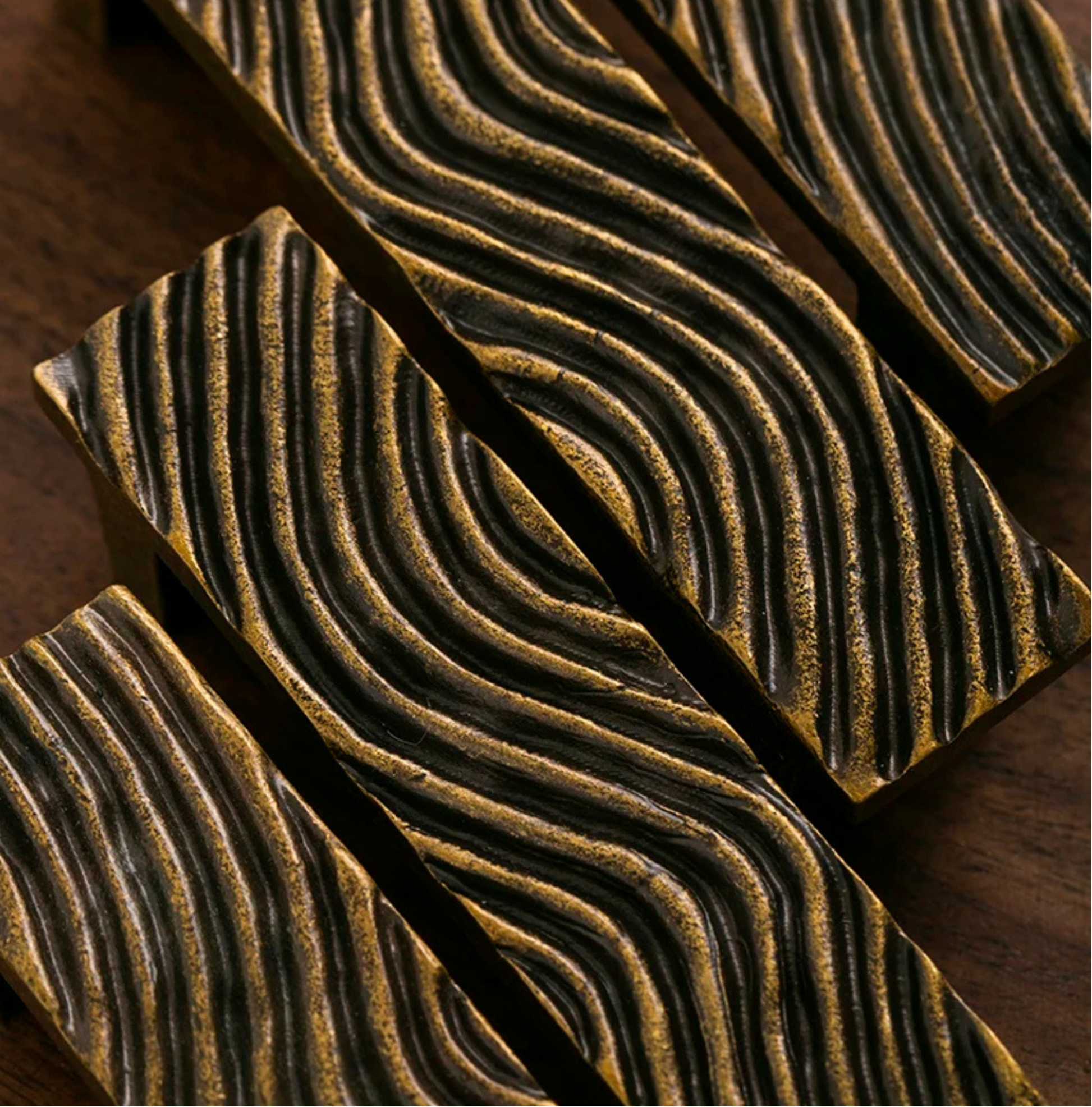Close-up of textured gold handles arranged diagonally on a dark wooden background.