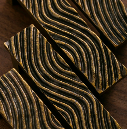 Close-up of textured gold handles arranged diagonally on a dark wooden background.