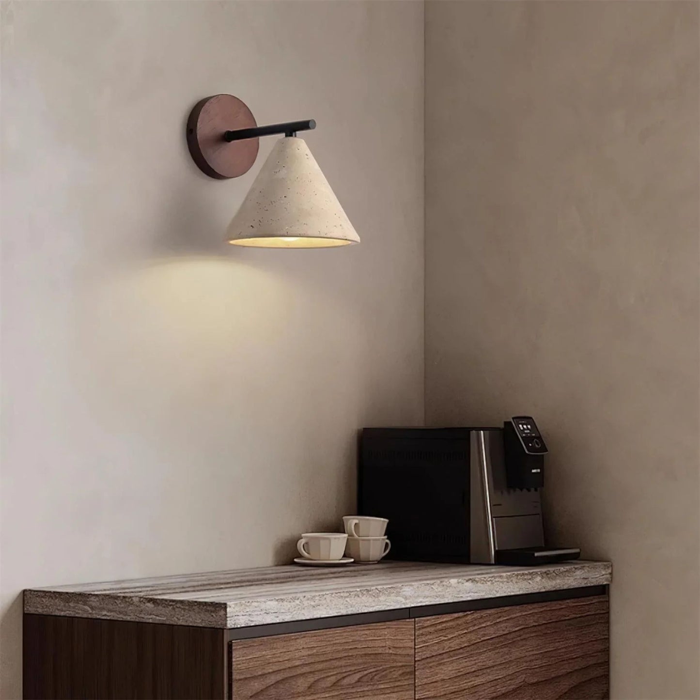 A warm-lit wall sconce with a wood backplate and angled white shade mounted on a beige wall in a cozy room.