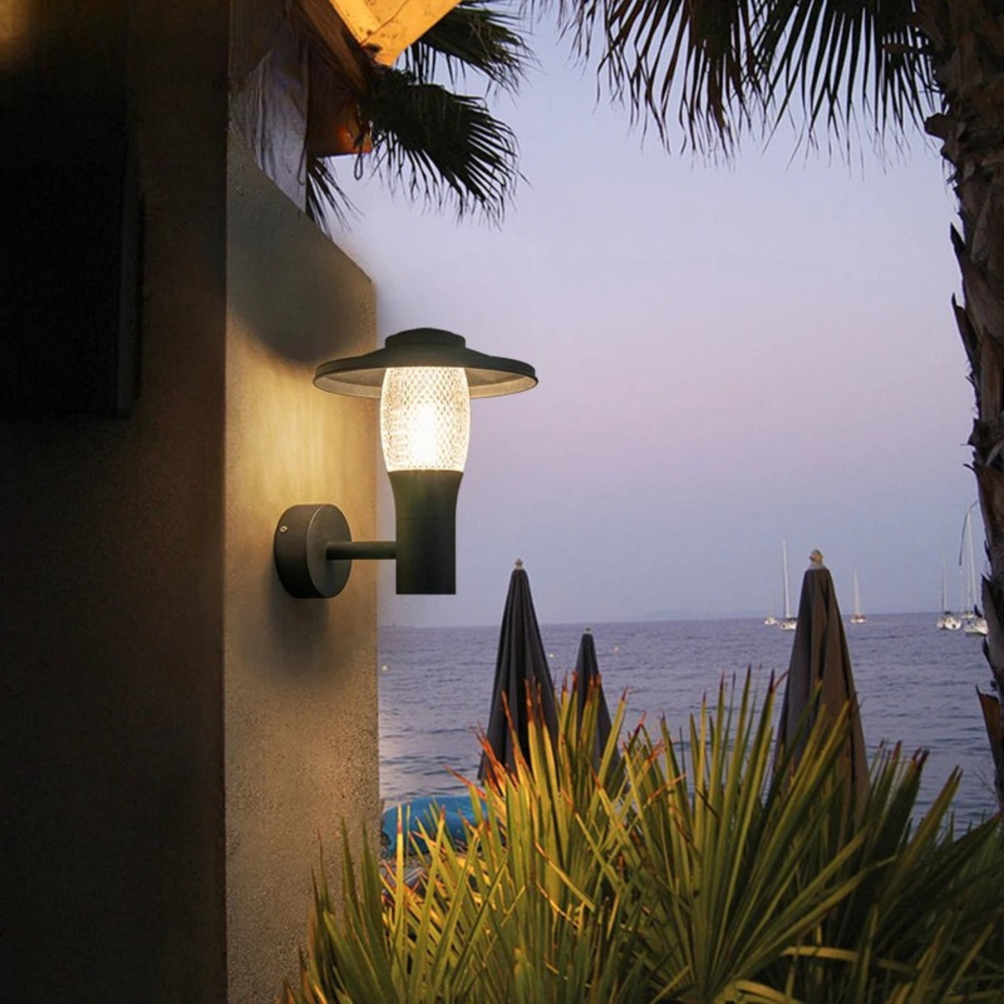 Modern outdoor sconce lighting up a tropical patio with sea view at dusk.